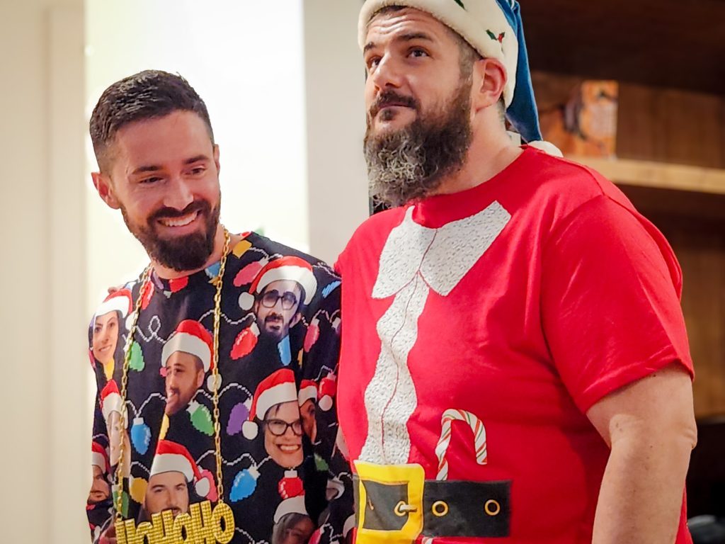 President Brandon Mogan and Principal Advisor Samuel Zammarrelli at Tora's Christmas party. Brandon is wearing a sweatshirt with the faces of Tora staff in Santa hats printed on it, and Samuel is wearing a Santa-themed t-shirt.