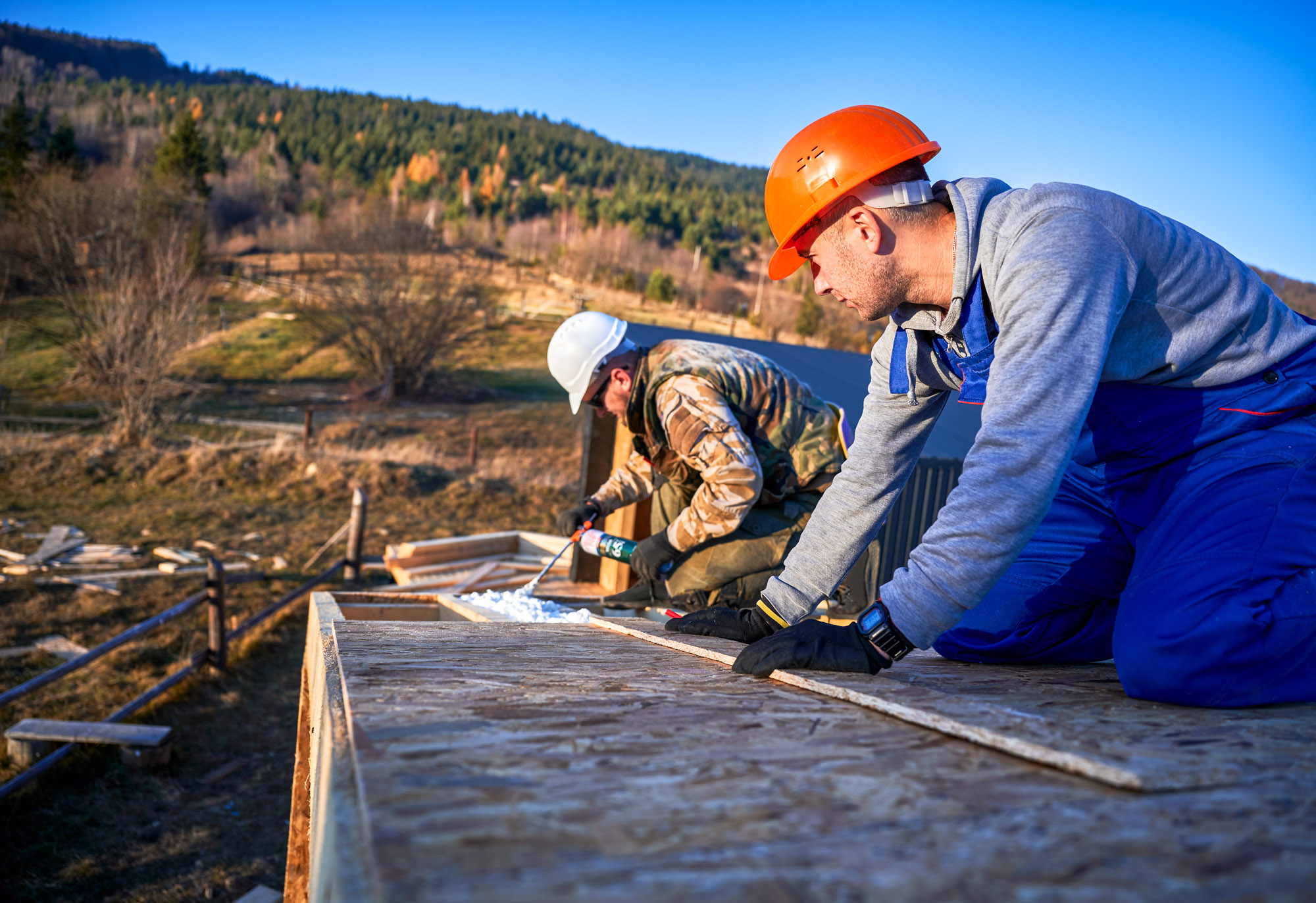 Male builder doing thermal insulation on roof of wooden frame house. Man worker spraying polyurethane foam on rooftop of future cottage. Construction and insulation concept.