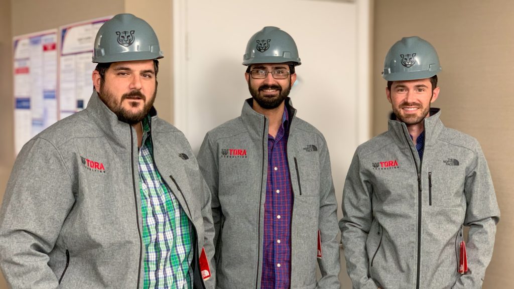Principal Advisors Samuel Zammarrelli and Sanjam Singh with President Brandon Mogan wearing Tora hard hats at an environmental compliance client site.